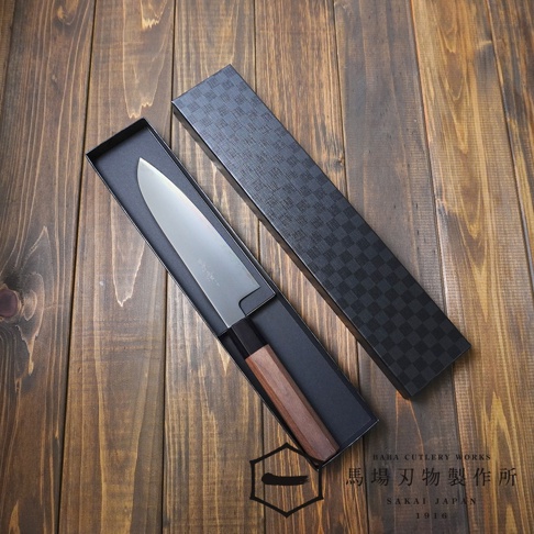 [景清] Chromax鋼三德刀，刀身為金屬銀色，配有胡桃木色手柄，置於黑色收納盒內，盒蓋為黑色格紋設計，整體擺放在木紋桌面上。