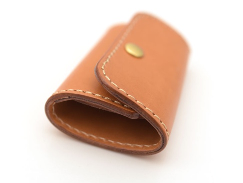 淺棕色皮革手作鑰匙包，帶有六個掛鉤，正面有一個金色按扣，邊緣有縫線裝飾。