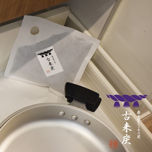 古來炭方形調濕木炭四件組，包含一個帶有日文標籤的白色透氣袋，袋內為黑色木炭顆粒，以及一個黑色方形底座和銀色金屬鍋。