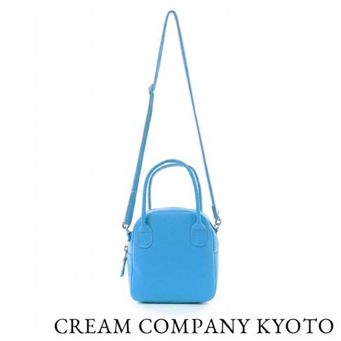 這款由 CREAM COMPANY KYOTO 出品的亮藍色牛皮貝殼包，設計簡約精緻，配有雙提把與可拆式肩背帶，呈現手提與單肩兩用的多功能設計，展現京都職人手作的質感與輕量耐用的特性。