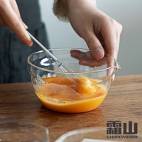 日本霜山品牌耐熱玻璃調理碗，包含導流口設計，碗中盛有蛋液，正由一人使用打蛋器攪拌。