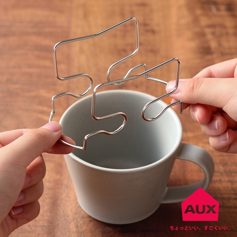 銀色金屬線材製成的可調式耳掛咖啡專用架，由兩隻手持握，準備架設在一個灰色馬克杯上方。