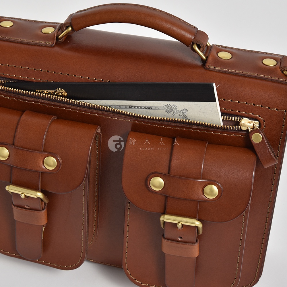 棕色皮革雙口袋兩用單肩包，正面有兩個帶有銅扣的翻蓋口袋，上方有一個拉鍊主隔層，內部可見文件。