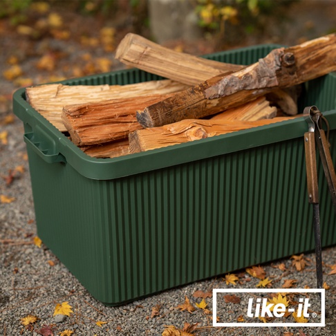 一個綠色的可疊式波浪紋收納箱，裡面裝有木柴，箱子側面有提把，邊緣有波浪紋設計。