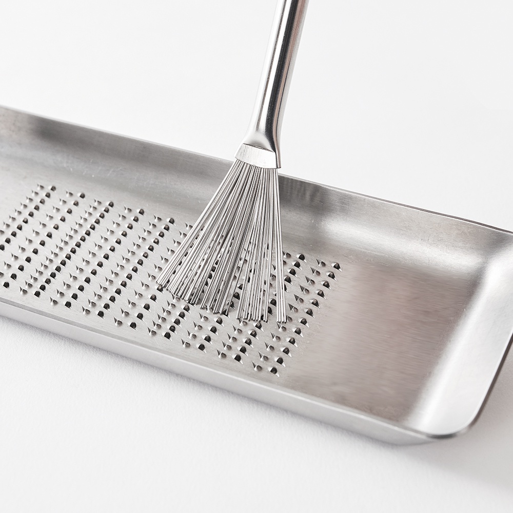日製料理小刷，銀色金屬材質，刷頭由多支細長的金屬絲組成，用於清潔刨絲器上的細小殘渣，搭配同為銀色金屬製的長方形刨絲器。