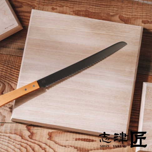 一個帶有鋸齒刀刃的麵包刀放在一個淺色木製砧板上，砧板放在木紋背景上。