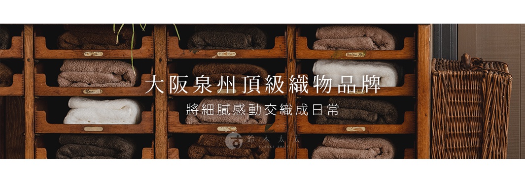 木製層架整齊擺放著數條素面毛巾，顏色包含深棕、淺棕、米白等。毛巾質地蓬鬆，呈現簡約、自然的風格。