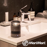 一個深灰色圓柱形無線藍牙音響，頂部有透明燈罩，內有黃色LED燈。音響側面有MoriMori品牌標誌，底部有「ON/OFF LED」和「ON/OFF」按鈕，以及藍牙圖示。