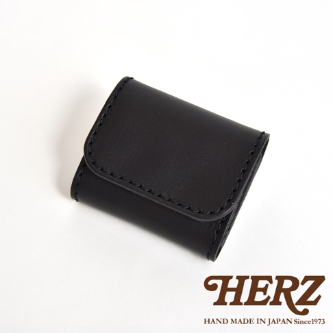 一個日本HERZ品牌製作的黑色皮革雙折收納零錢包，以俯視角度呈現，採用厚實皮革與精緻縫線設計，右下方印有品牌名稱與手工製造資訊。