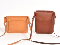 兩款職人手作皮革直式隨行袋，一為淺棕色，一為深棕色。皆為直立式設計，正面有一個方形外插袋，袋蓋上方有品牌壓紋。材質為皮革，整體風格簡約。