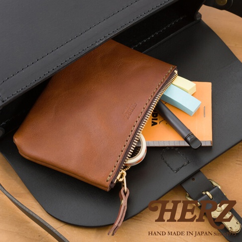 職人手作棕色皮革長方形拉鍊收納包，拉鍊處有皮革拉環，包內有筆記本和彩色便利貼。