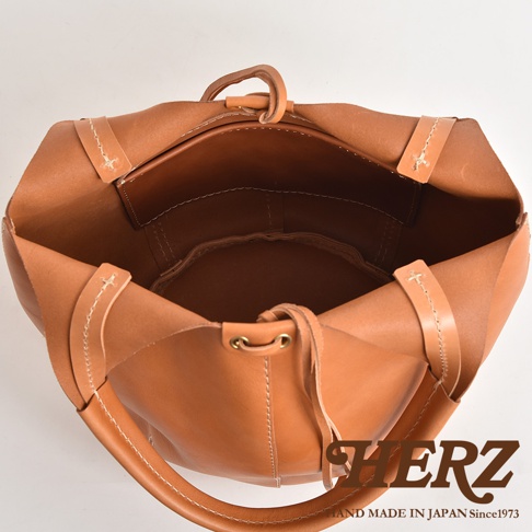 職人手作皮革球形肩掛托特包，採用天然皮革材質，呈現大地色調。包款為開放式設計，內部有分隔層，搭配皮革提把與肩帶，展現簡約的日系風格。