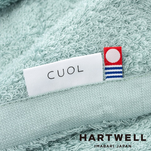 細緻淺綠色毛巾，表面絨毛柔軟，帶有「CUOL」品牌織標及紅底白圓點、藍白條紋裝飾織標。