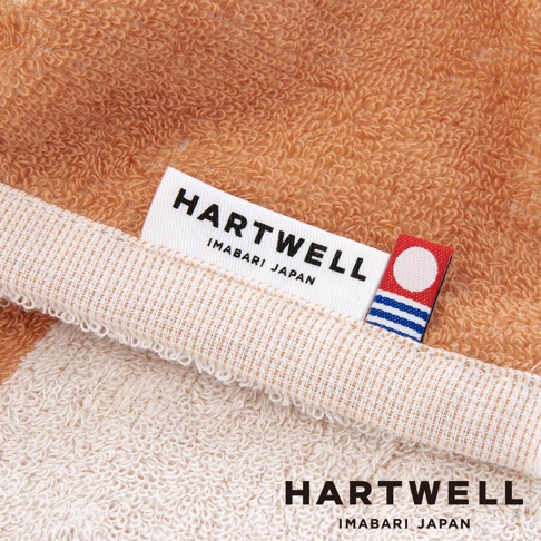 今治毛巾特寫，展示其柔軟紋理，並帶有「HARTWELL IMABARI JAPAN」品牌標籤，以及印有紅色圓點和藍色條紋的裝飾小標籤。