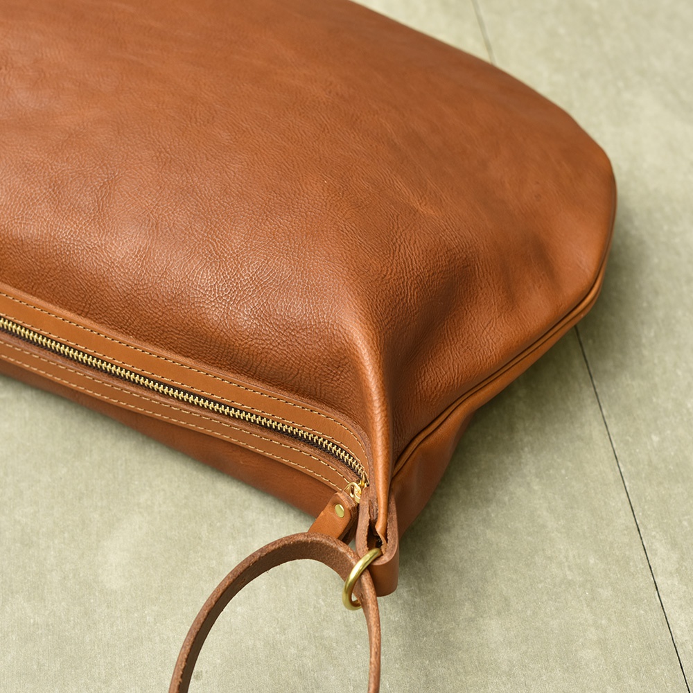 一個棕褐色的皮革單肩包，半月形設計，帶有金色拉鍊和皮革肩帶。