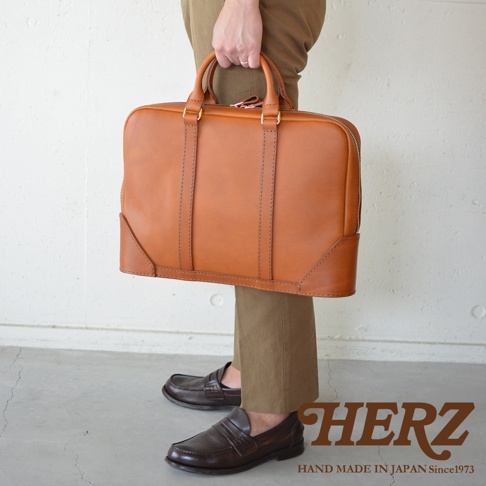 職人手作咖啡色皮革Organ商務公事包，配有雙提把和拉鍊封口，皮革材質，整體呈現簡約大方的設計。