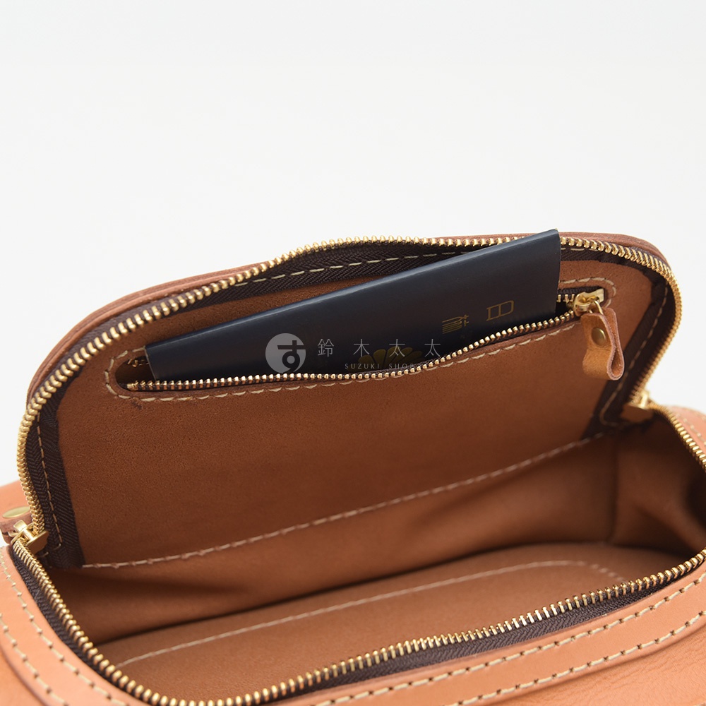 皮革包內部，拉鍊打開，露出一個放有卡片或小冊子的夾層，卡片上印有日文文字和品牌標誌。