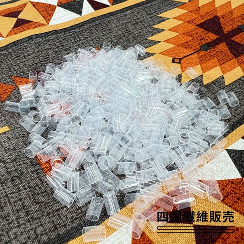 這是一張俯視拍攝的照片，呈現了大量半透明的白色塑膠小軟管，這些小軟管通常用於枕頭填充物，背景為帶有幾何圖案的民族風布料，右下方印有四國纖維販賣的文字標示。