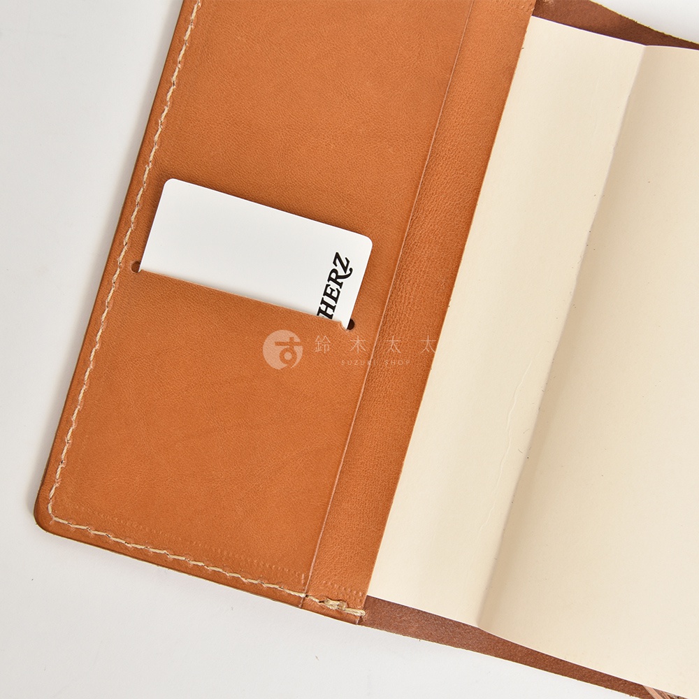 職人手作皮革手帳書套，卡夾處有一個白色的卡片，上面印有HERZ字樣。