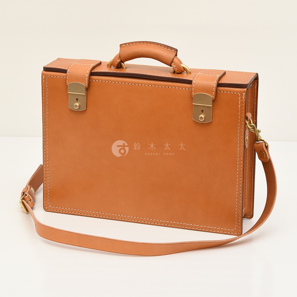 淺棕色皮革兩用機師箱，有頂部提把、黃銅色金屬鎖扣、可拆卸肩帶，以及精緻的縫線細節。