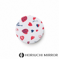 白色圓形化妝鏡，表面印有紅色和藍色的小圓點草莓圖案、紅色愛心圖案、藍色文字「plume.」和「love」，以及條紋愛心圖案。