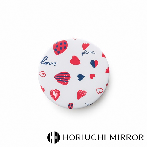 白色圓形化妝鏡，表面印有紅色和藍色的小圓點草莓圖案、紅色愛心圖案、藍色文字「plume.」和「love」，以及條紋愛心圖案。