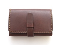 職人手作深棕色皮革名片收納夾，帶有腰帶式翻蓋設計，側面以粗線縫製，質感經典。