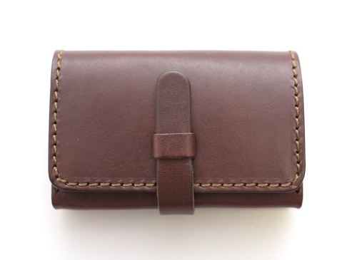 職人手作深棕色皮革名片收納夾，帶有腰帶式翻蓋設計，側面以粗線縫製，質感經典。
