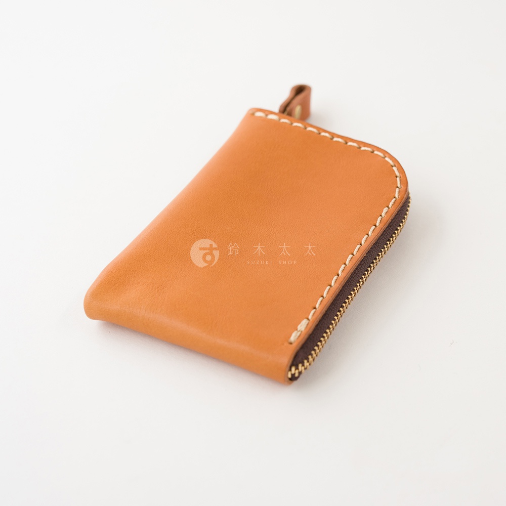 這是一個淺棕色皮革製作的迷你拉鍊錢包，採用耐用的手工縫線工藝，側面設有拉鍊開口與皮革拉環，表面印有鈴木太太的品牌圖標，整體外觀簡約精緻。