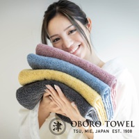 五條不同顏色的毛巾堆疊，包括深灰色、黃色、藍色和粉紫色，質地柔軟蓬鬆。