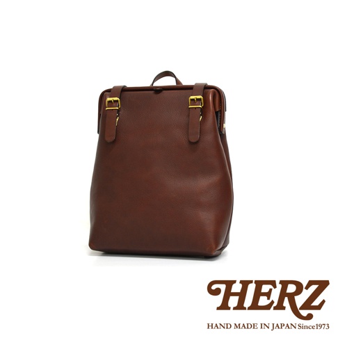 咖啡色皮革後背包，設計簡約，有兩個皮質帶子搭配金色金屬扣環，整體風格復古。