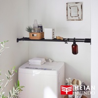 黑桿兩段式強化伸縮桿，固定在白色牆壁上，上方架子上擺放著清潔用品、藤編籃和白色收納盒，下方是白色洗衣機，有折疊毛巾和一個懸掛的棕色噴霧瓶。