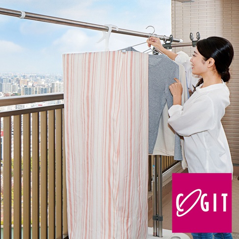 一名女子在陽台使用360°輕鬆旋轉卡扣式通風晾曬架，掛上衣物。晾曬架為金屬材質，附有白色布簾，布簾上有粉色細條紋。
