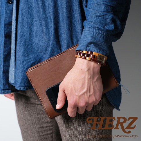 職人手作皮革B6記事本書套，深棕色皮革，搭配牛仔襯衫與斜紋長褲，手腕佩戴木質錶帶手錶。