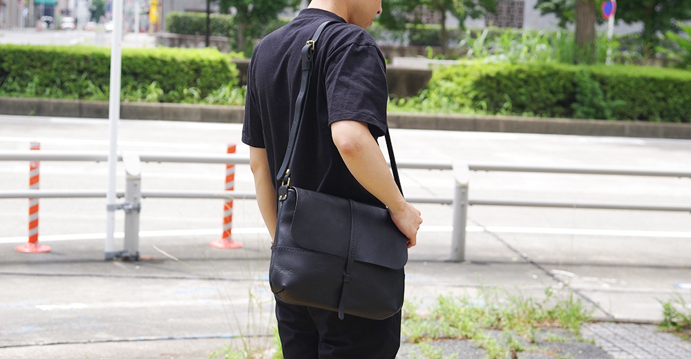 身穿黑色T恤的男子，斜背一個黑色的皮革馬鞍包。