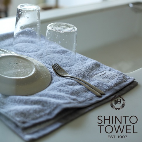 灰色蓬厚迷你浴巾，材質為有機棉，上面放著兩個有水珠的玻璃杯、一個白色盤子和一把叉子。