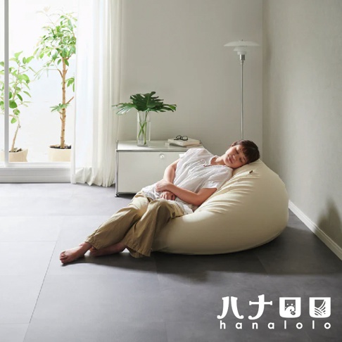 淺米色皮革款懶骨頭沙發，一個人舒適地躺臥其中，背景為簡潔的居家空間，有落地窗、綠植與落地燈。