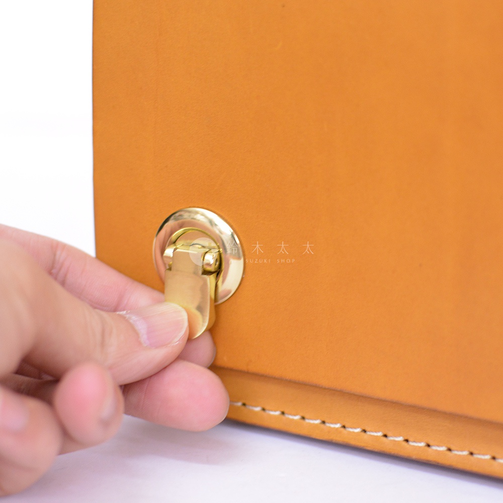 職人手作皮革經典兩用雙扣迷你單肩包，展示其黃褐色皮革本體及金色金屬鎖扣，手部特寫示範如何操作鎖扣。
