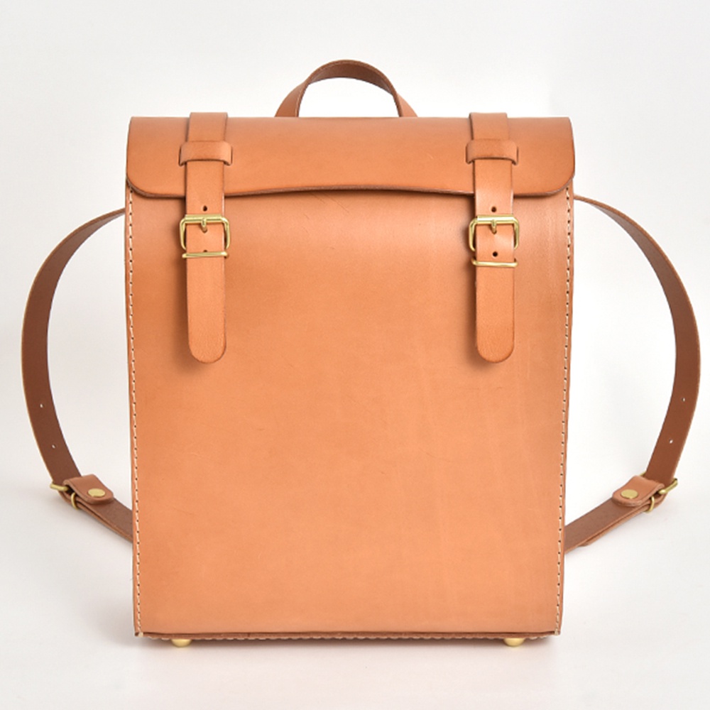 職人手作皮革後背包 R-31 (厚實版)，採用天然皮革材質，呈現溫潤的淺棕色調。包款設計簡約，設有兩個前方皮帶扣與金屬釦環，搭配雙肩背帶，展現復古風格。