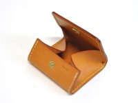 淺棕色皮革製成的箱型零錢包，打開狀態，露出內部空間，有金色按扣及品牌標誌。