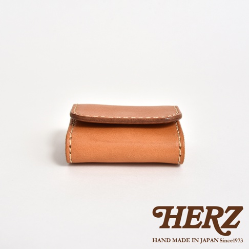 日本HERZ職人手作皮革零錢包，呈現簡約的棕色皮革質感，採用雙折式設計並搭配精緻的縫線細節，整體採正面水平視角拍攝，右下方印有品牌標誌與手工產地說明。