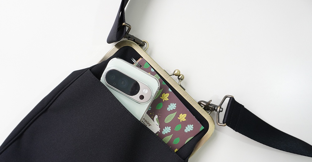 黑色斜背包內裝有手機和一張印有楓葉圖案的卡片，肩帶為黑色。