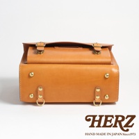 職人手作皮革橫式書包，淺棕色皮革，帶有金色釦環與铆釘，整體呈現復古風格，底部兩側有D型環設計。