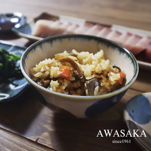 筆青釉繪深型飯碗，內盛有香菇、紅蘿蔔等配料的炊飯。飯碗邊緣飾有青釉圓點圖案，器身為陶瓷材質。
