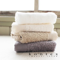 PRIMAVERA 超細纖純棉素面浴巾疊放，顯示白色、米白色、淺棕色和灰色四種顏色，質地蓬柔。