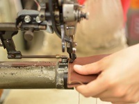 職人手作皮革存摺文件收納夾，棕色皮革，正在使用工業縫紉機進行縫製，展示製作過程。