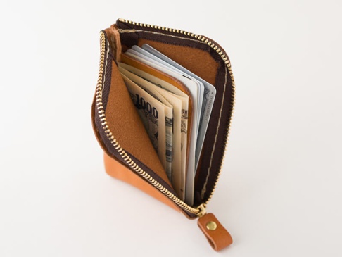 棕色皮革迷你錢包，拉鍊部分有金屬拉頭，錢包內有日圓和美元紙鈔，以及幾張卡片。