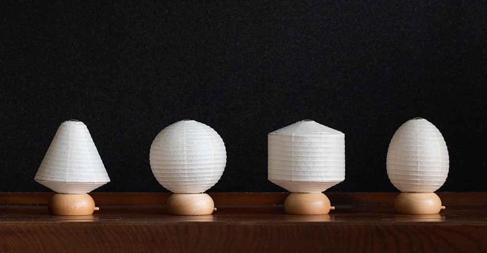 四個無印風格的迷你紙質裝飾提燈，由白色皺紋紙製成，底座為淺色木頭，造型分別為錐形、圓球形、圓柱形和蛋形。
