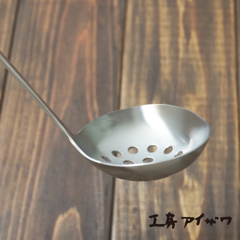 銀色不鏽鋼萬用瀝水湯勺，勺面有圓形濾孔，勺柄細長，置於木紋背景上。