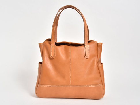 職人手作皮革直式肩背托特包，採用光滑淺棕色皮革製成，具有雙提把、外部側袋和縫線細節。